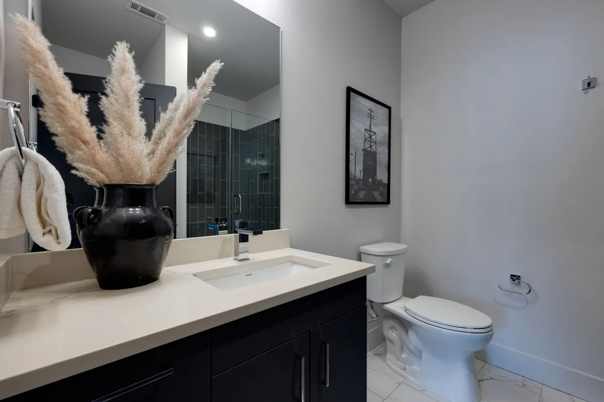 A modern bathroom setting with a sleek vanity and sink, black vase with pampas grass, and framed artwork, creating a calm and spa-like atmosphere.