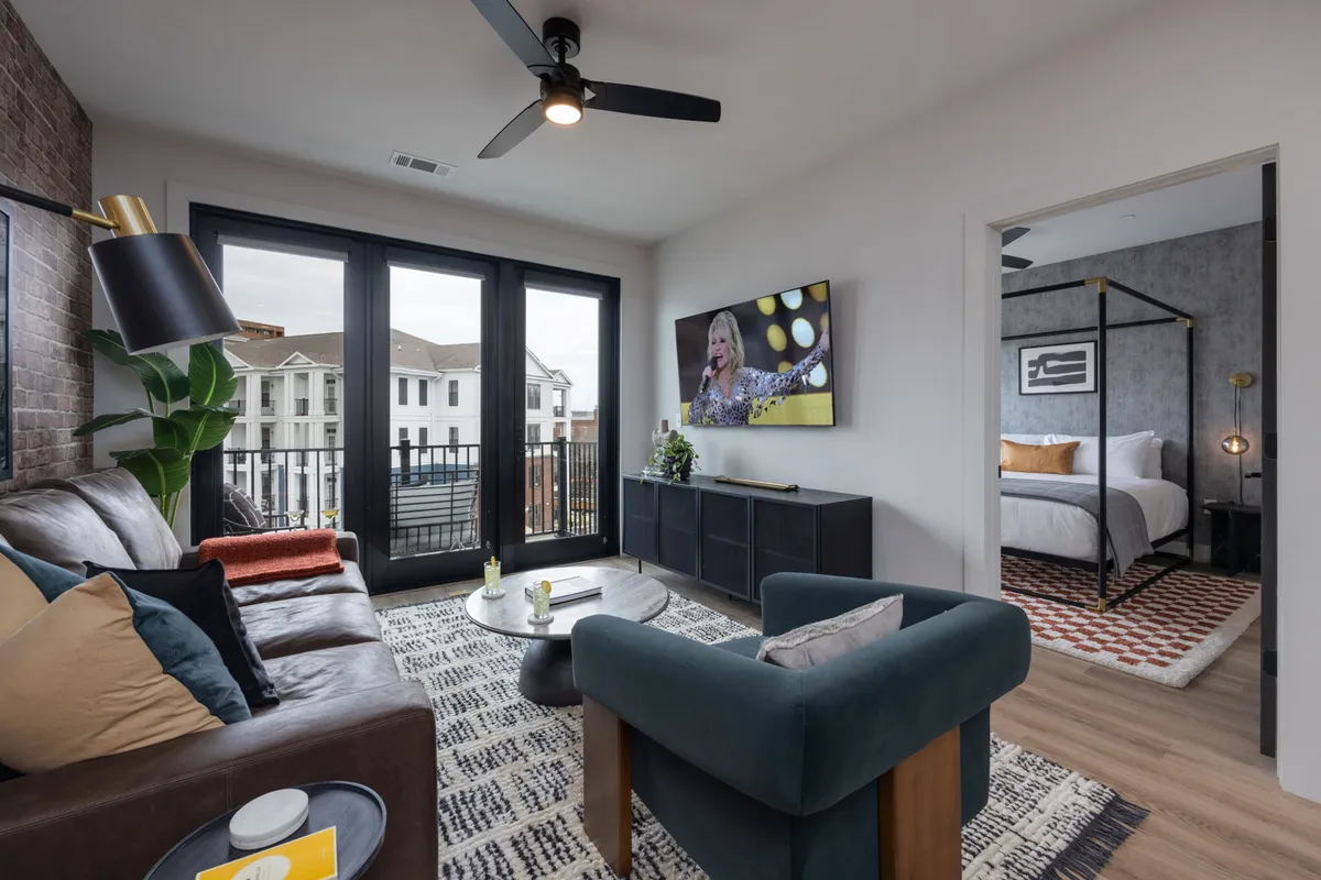 A cozy and contemporary living room featuring a vibrant sofa with colorful cushions, a modern coffee table adorned with decorative items, and a large window offering an outdoor view. The television displays a lively image, reinforcing the room’s suitability for movie nights and casual gatherings.