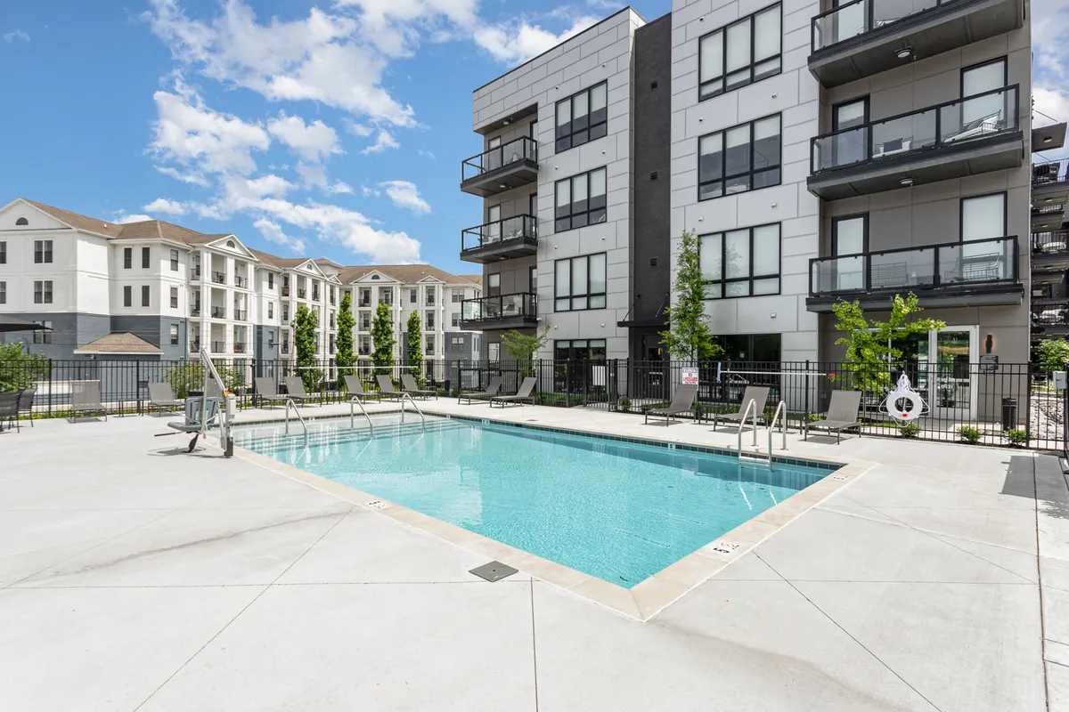 A tranquil exterior view of the resort-style swimming pool at Vesta, surrounded by landscaped trees and balconies. The relaxed poolside atmosphere communicates both leisure and fun, ideal for families looking to unwind after city adventures.