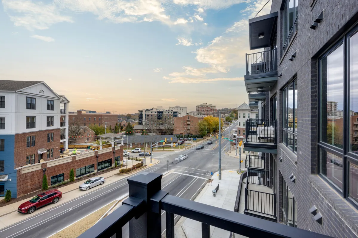 A perspective from the balcony railing looking out over nearby buildings and the distant city skyline. The street view below and the open, urban vista create a strong sense of place and emphasize the elevated, private vantage point.