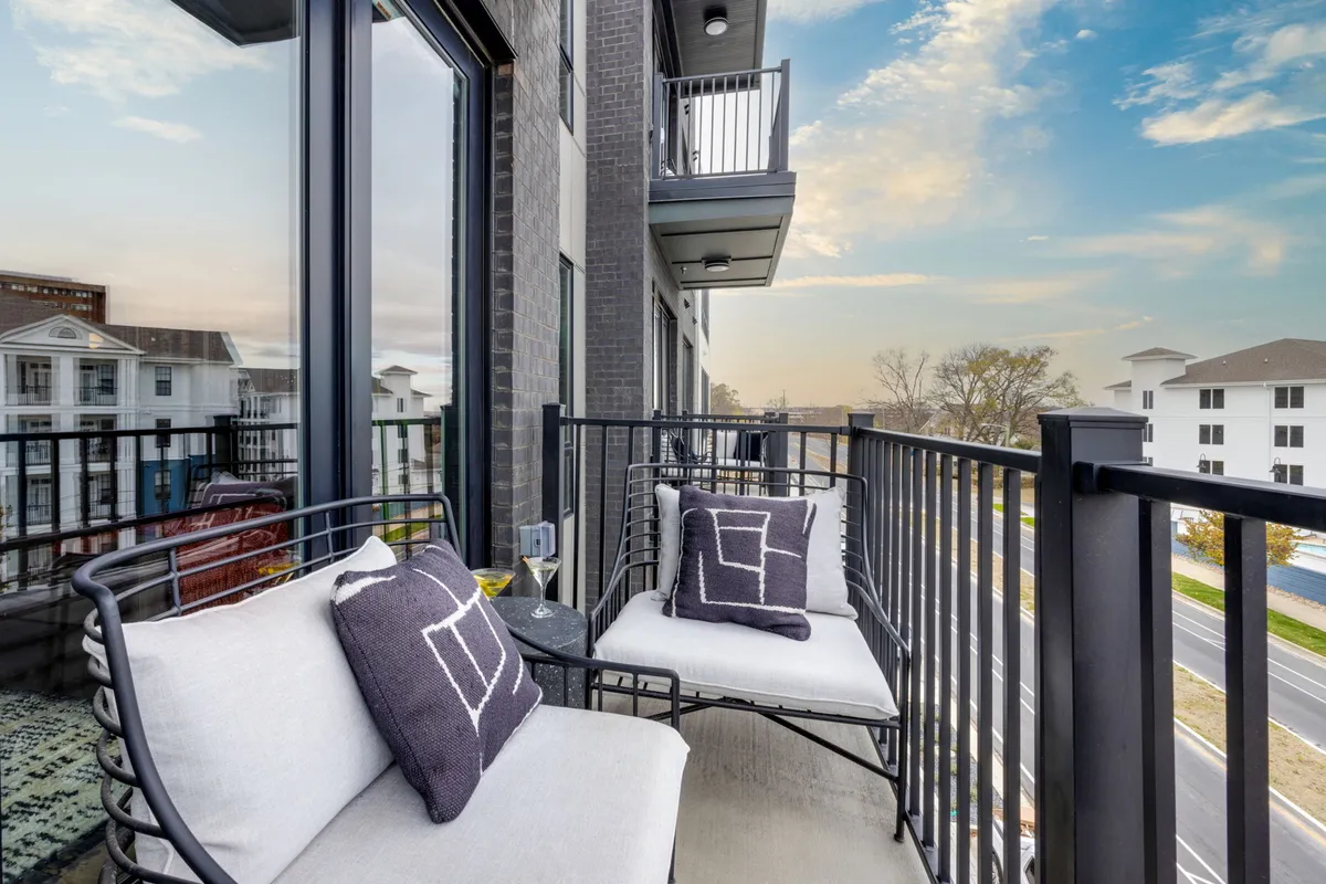 An inviting private balcony with comfortable seating and decorative pillows, offering an elevated cityscape view. The seating arrangement is cozy and ideal for enjoying drinks or conversations while taking in the scenic skyline, especially as the sun sets.