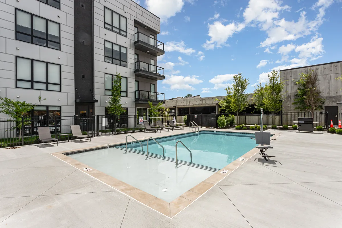 An inviting exterior shot of the building’s swimming pool, with lounge chairs and balconies visible above, surrounded by landscaped greenery. The scene exudes relaxation and leisure, balancing city energy with tranquil outdoor amenities.