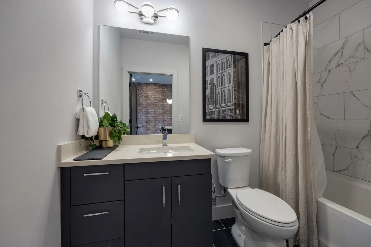 A bright bathroom featuring a vanity with sink, a large mirror, framed artwork, and a shower curtain suggesting a shower/tub combo, with welcoming light and organized space.
