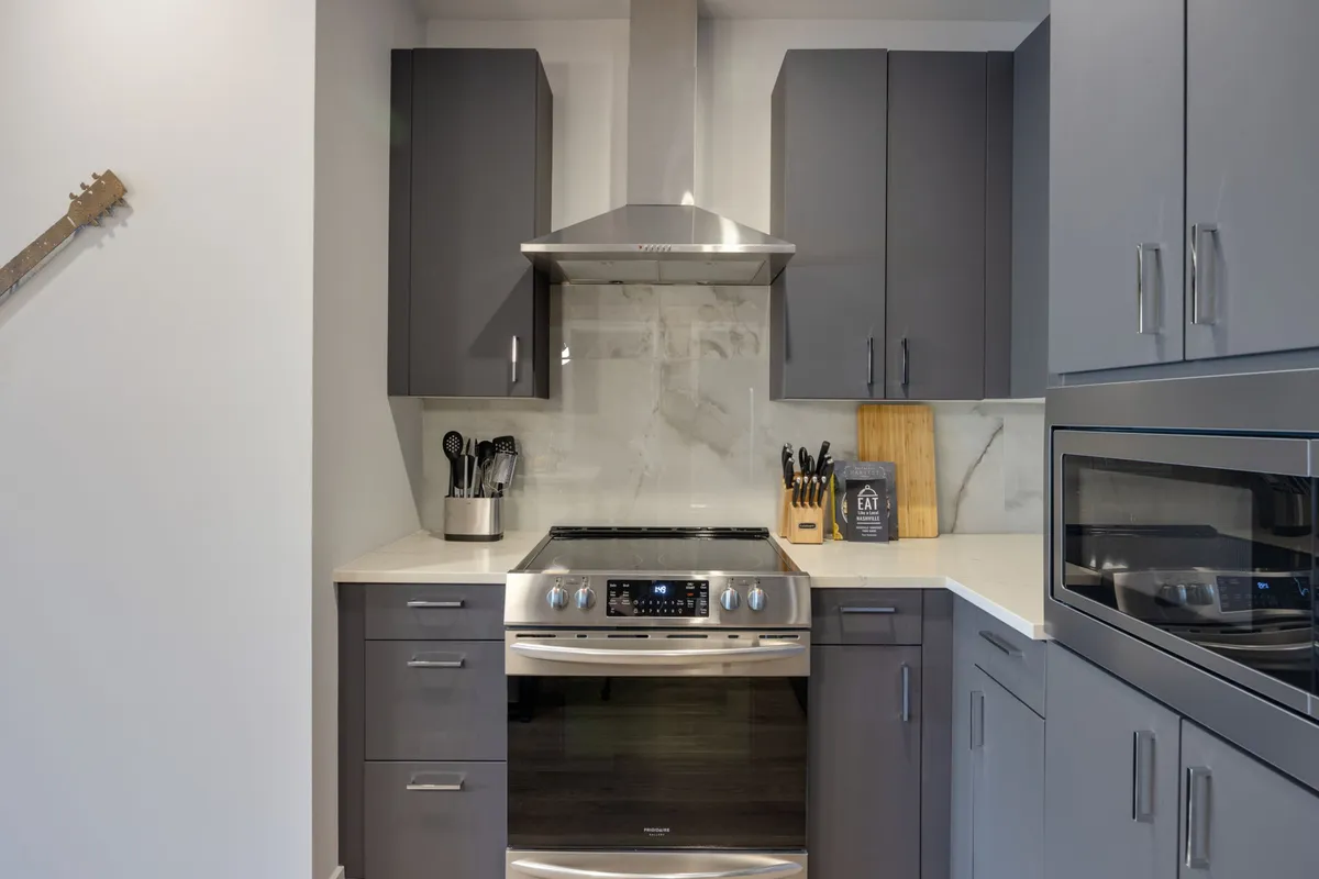 A sleek, fully equipped kitchen showcasing stainless steel appliances, gray cabinetry, a marble backsplash, and a variety of kitchen utensils. The design is both contemporary and functional, ideal for everything from quick breakfasts to elaborate dinners.